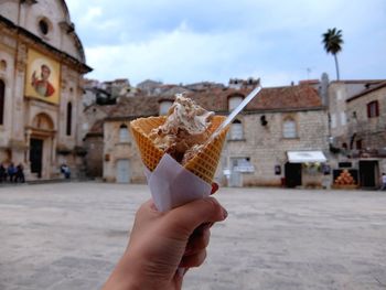 Cropped image of woman hand holding gelato ice cream on street against buildings