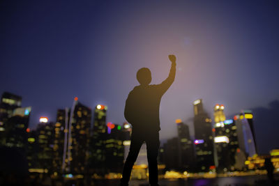 Rear view of man standing by illuminated cityscape against sky