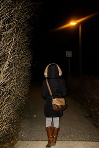 Rear view of woman with umbrella walking at night