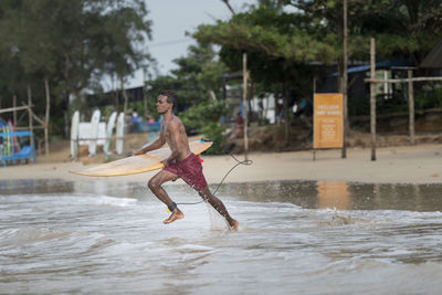 Shirtless man with surfboard running in sea