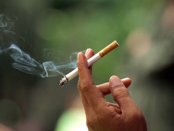 Close-up of human hand holding burning cigarette outdoors