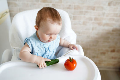 Cute baby girl sitting on high chair at home