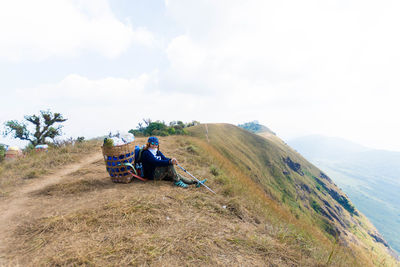 Full length of man with basket sitting on mountain against sky