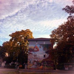 Trees in front of building against cloudy sky