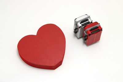 High angle view of red heart shape and miniature suitcases over white background