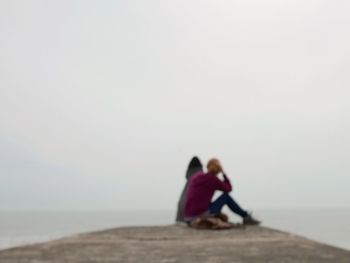 Couple sitting on beach against clear sky