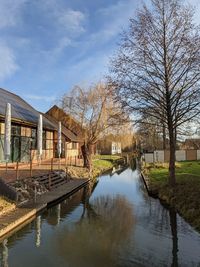 Canal amidst bare trees and buildings against sky