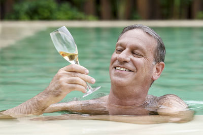 Smiling mature man holding champagne flute while leaning at poolside