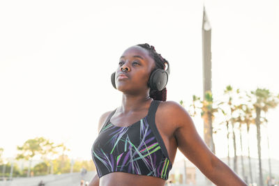 Fit black female athlete in sportswear and headphones standing outdoors against blurred background