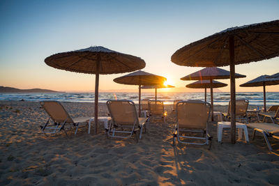 Umbrellas and chairs on beach against sky during sunset