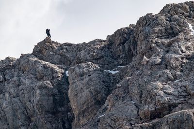Rear view of woman climbing on cliff against sky