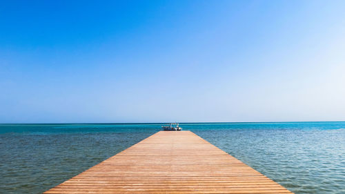 Pier over sea against clear blue sky