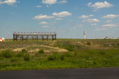 Grassy field by runway against sky