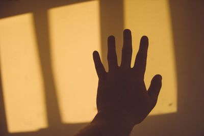 Close-up of human hand against sunlight on yellow wall