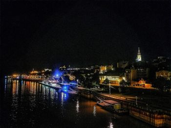 Illuminated buildings by river against sky at night