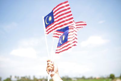 Low angle view of hand holding flag against sky