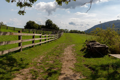 Wooden fence on green meadow with clouds in the background