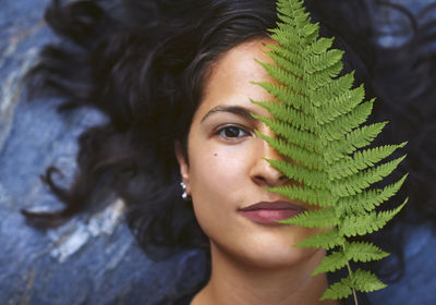 Woman with a fern on her face. she's lying on a rock and covers