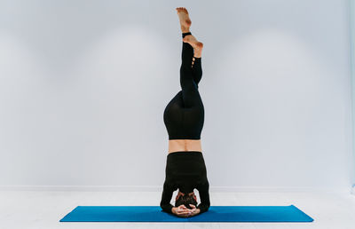 Full length of woman performing headstand against white background