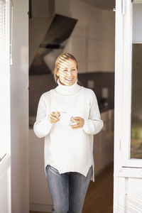 Happy mature woman with coffee cup leaving house