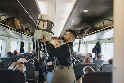 Side view of man helping family to load luggage on shelf in train