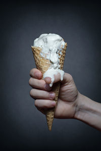 Close-up of hand holding ice cream cone against black background