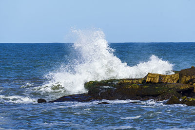 Waves splashing on sea against clear sky