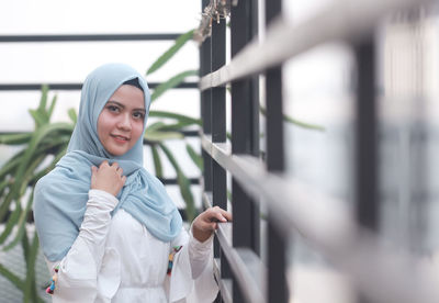 Portrait of smiling mid adult woman wearing hijab standing by metal