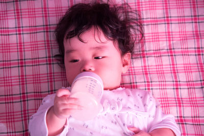 Close-up of cute baby holding milk bottle while lying on blanket