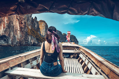 Rear view of woman sitting on boat in sea against sky