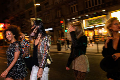 Group of stylish multiracial friends walking together on city street for party at night