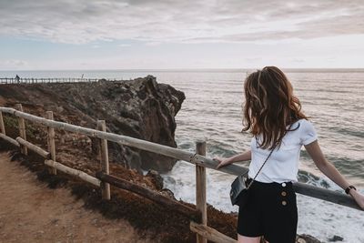 Woman leaning on railing by sea during sunset