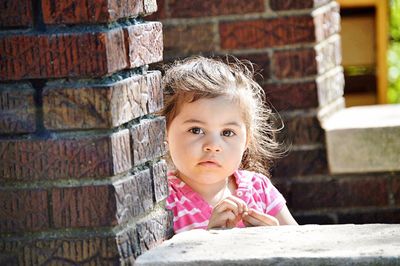 Portrait of cute girl standing by brick wall