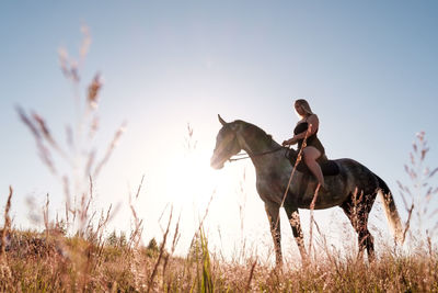 Young man riding horse on field against sky