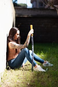 Side view full length of woman holding sword while sitting on field