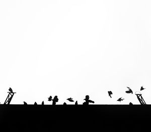 Low angle view of silhouette birds perching against clear sky