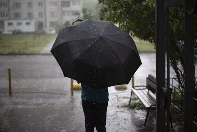 Rear view of person with umbrella walking in rain during rainy season