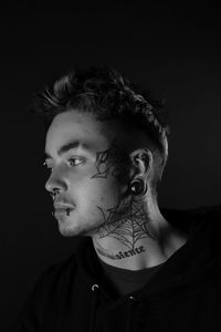 Portrait of young man with tattoos against black background