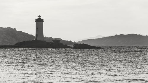 Monochrome landscape of lighthouse on the rocks and mountain on background during sunset