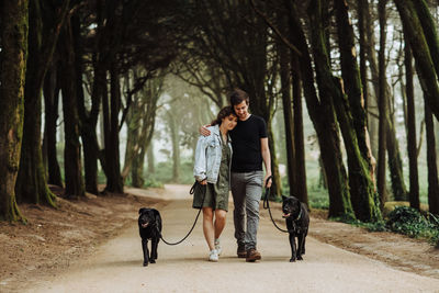 Couple embracing while walking dogs on a leash down a road in forest