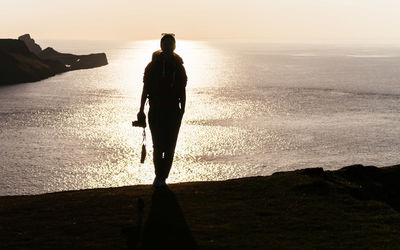 Rear view of silhouette man standing at beach during sunset