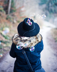 Rear view of woman wearing hat and fur coat by bubbles in mid-air