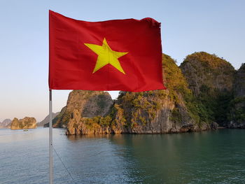 Red flag on rock by sea against sky