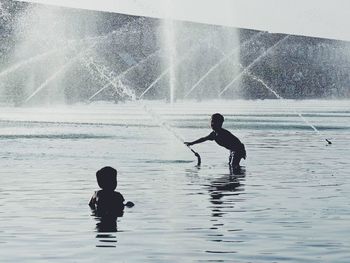 Silhouette men in sea against sky