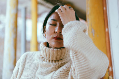 Young woman with eyes closed standing against wall