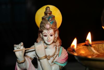 Close-up of lit diya by krishna statue