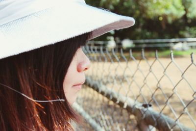 Close-up of young woman standing by chainlink fence at park