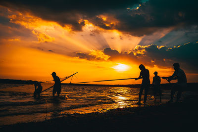 Silhouette people on beach against sky during sunset