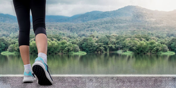 Low section of woman wearing sports shoes and socks while standing by lake