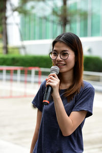 Female journalist with microphone standing against building